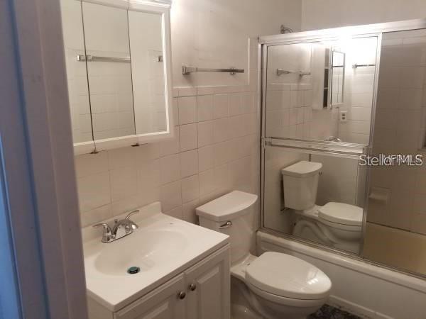 4061 Kirkland Blvd, Orlando, FL 32811 - full bathroom featuring tile walls, toilet, bath / shower combo with glass door, and vanity