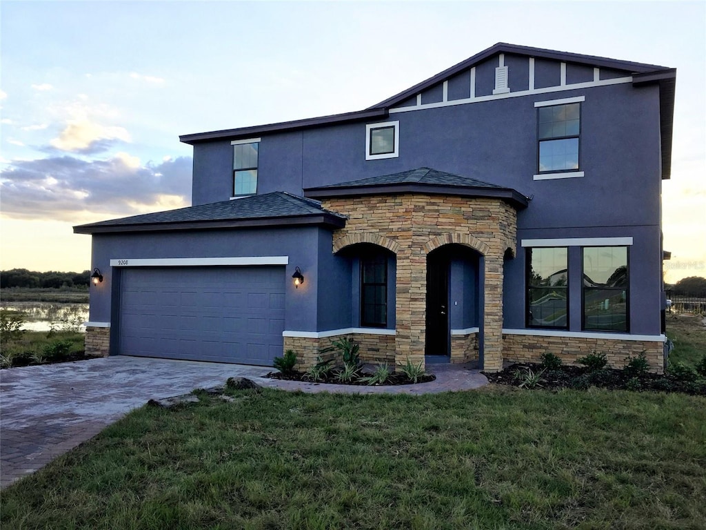 view of front facade with stucco siding, stone siding, a front yard, an attached garage, and driveway