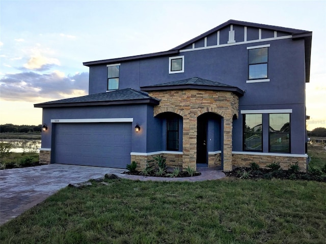 view of front facade with stucco siding, stone siding, a front yard, an attached garage, and driveway