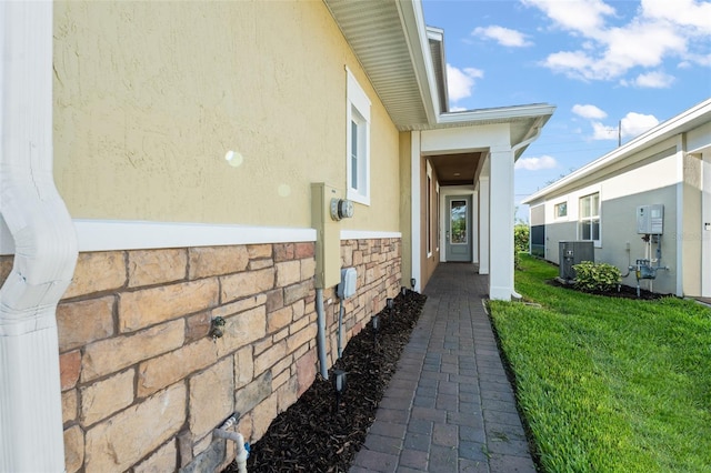 view of exterior entry with cooling unit, a yard, and stucco siding