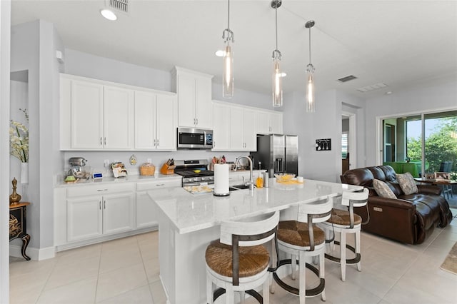 kitchen with stainless steel appliances, open floor plan, white cabinetry, a kitchen breakfast bar, and light tile patterned flooring
