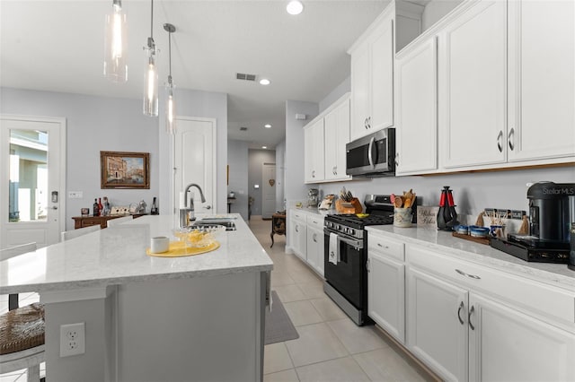 kitchen with appliances with stainless steel finishes, a sink, an island with sink, light tile patterned floors, and white cabinets