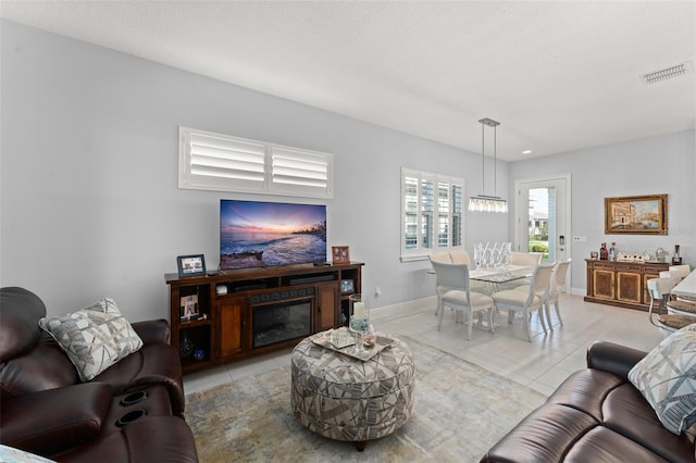 living area featuring light tile patterned floors, baseboards, and a glass covered fireplace