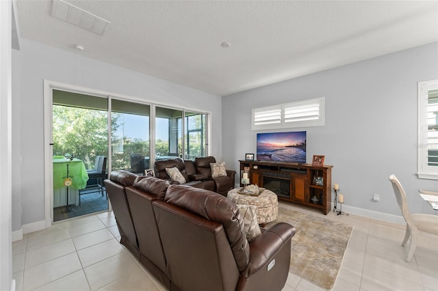living area featuring healthy amount of natural light, light tile patterned floors, baseboards, and a textured ceiling