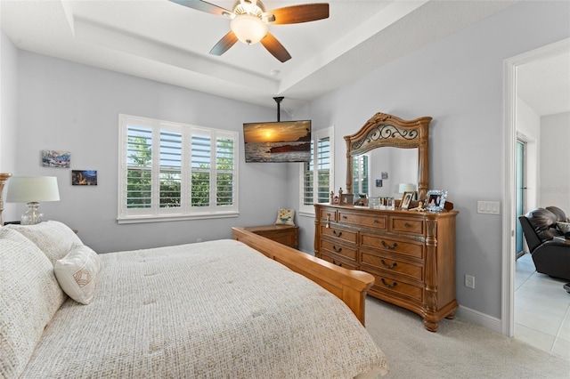 bedroom with light colored carpet, a ceiling fan, a tray ceiling, and baseboards