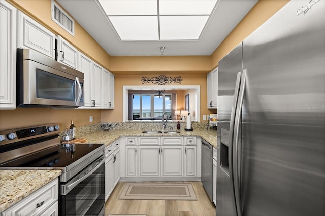 kitchen featuring stainless steel appliances, a sink, white cabinetry, light wood finished floors, and light stone countertops