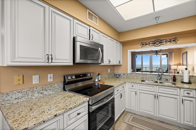kitchen with stainless steel appliances, a sink, white cabinetry, a water view, and light stone counters