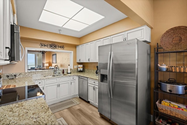 kitchen with stainless steel appliances, a sink, white cabinets, light wood-type flooring, and light stone countertops