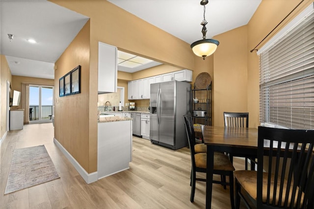 kitchen featuring appliances with stainless steel finishes, white cabinets, light wood-style flooring, hanging light fixtures, and a sink