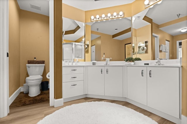 full bathroom with wood finished floors, a shower stall, double vanity, toilet, and baseboards