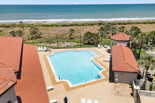 community pool with fence, a patio, and view of water and beach