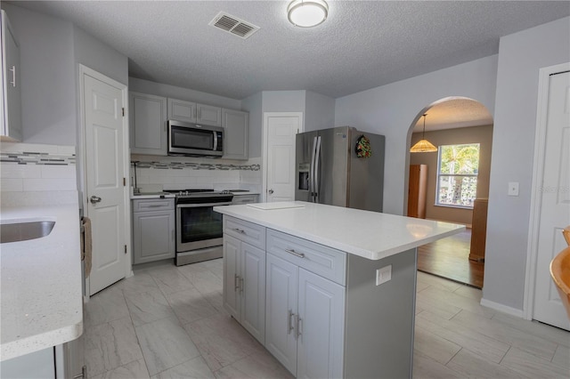 3216 White Blossom Ln, Clermont, FL 34711 - kitchen with appliances with stainless steel finishes, gray cabinetry, arched walkways, a kitchen island, and decorative backsplash