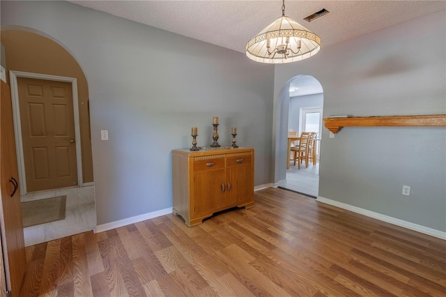 3216 White Blossom Ln, Clermont, FL 34711 - dining space with arched walkways, light wood-style flooring, a textured ceiling, and a chandelier