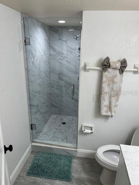 4453 S Atlantic Ave Unit 602, Ponce Inlet, FL 32127 - full bathroom with baseboards, vanity, toilet, a shower stall, and a textured ceiling