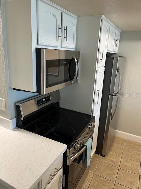 4453 S Atlantic Ave Unit 602, Ponce Inlet, FL 32127 - kitchen featuring appliances with stainless steel finishes, white cabinets, light tile patterned floors, and baseboards
