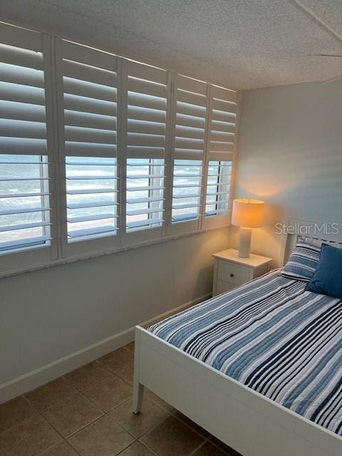 4453 S Atlantic Ave Unit 602, Ponce Inlet, FL 32127 - bedroom with tile patterned floors, multiple windows, a textured ceiling, and baseboards