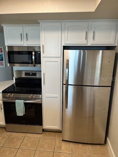 4453 S Atlantic Ave Unit 602, Ponce Inlet, FL 32127 - kitchen with stainless steel appliances, light countertops, light tile patterned flooring, white cabinetry, and baseboards
