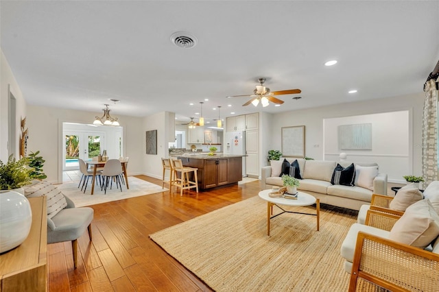 living area with a chandelier, a ceiling fan, light wood-style floors, recessed lighting, and baseboards