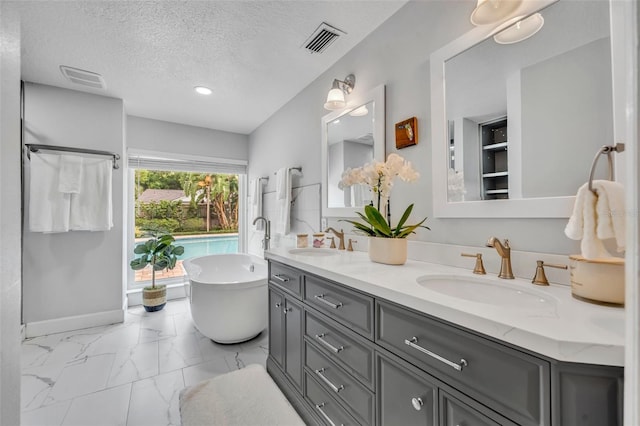 full bath with a textured ceiling, double vanity, a soaking tub, marble finish floors, and baseboards