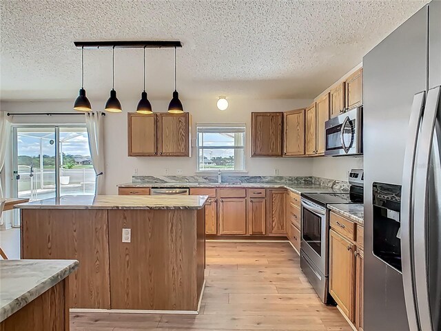 2384 Andrews Valley Dr, Kissimmee, FL 34758 - kitchen featuring appliances with stainless steel finishes, light wood finished floors, a textured ceiling, a kitchen island, and decorative light fixtures