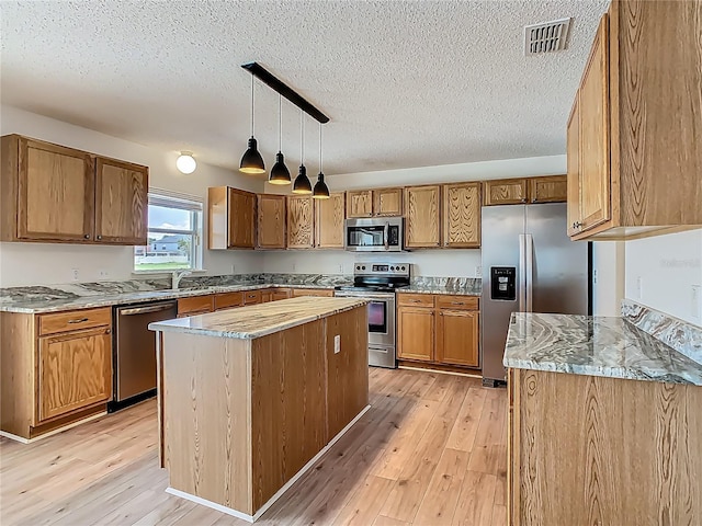 2384 Andrews Valley Dr, Kissimmee, FL 34758 - kitchen with appliances with stainless steel finishes, a textured ceiling, light wood-style floors, brown cabinets, and hanging light fixtures