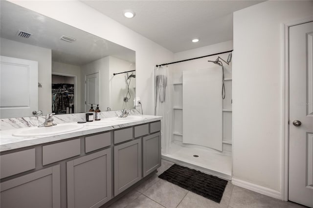 bathroom featuring tile patterned floors, a shower with shower curtain, a walk in closet, double vanity, and baseboards