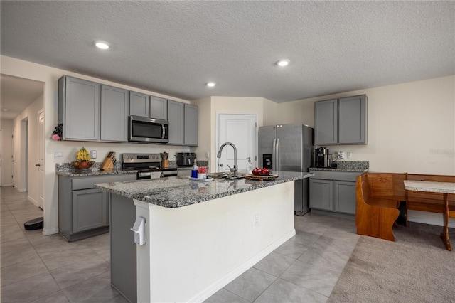 kitchen with stainless steel appliances, gray cabinetry, light tile patterned floors, dark stone countertops, and a textured ceiling