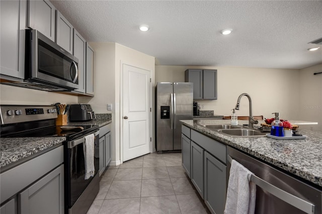 kitchen featuring appliances with stainless steel finishes, a sink, gray cabinets, a textured ceiling, and light stone counters