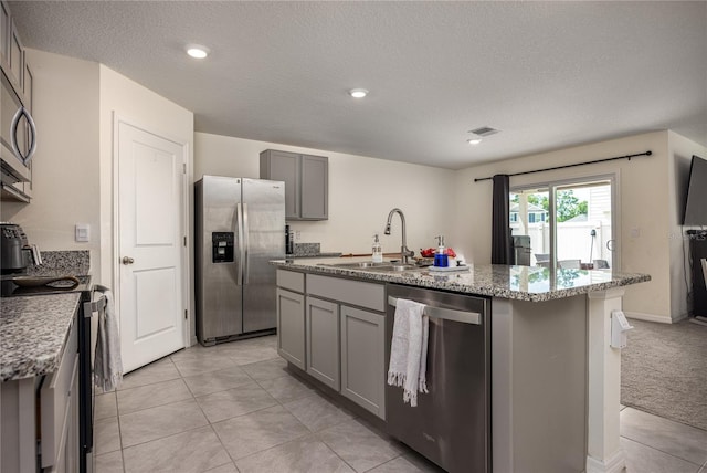 kitchen featuring appliances with stainless steel finishes, gray cabinets, a sink, a kitchen island with sink, and a textured ceiling