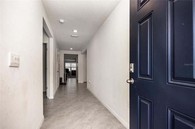 hallway featuring light tile patterned floors, a textured ceiling, baseboards, and recessed lighting