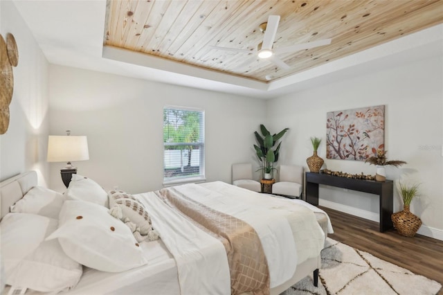 bedroom featuring a raised ceiling, wooden ceiling, wood finished floors, baseboards, and ceiling fan