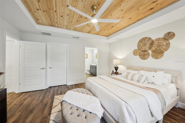 bedroom with a tray ceiling, wooden ceiling, wood finished floors, ensuite bathroom, and baseboards