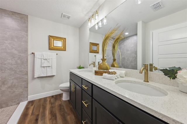 bathroom with baseboards, wood finished floors, toilet, double vanity, and walk in shower
