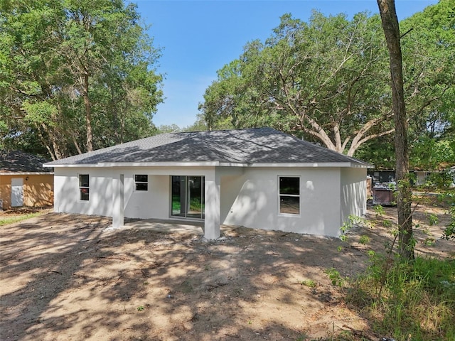 back of house with stucco siding and roof with shingles