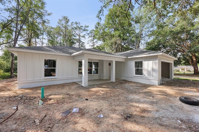 view of front of home with board and batten siding, an attached garage, a shingled roof, and dirt driveway