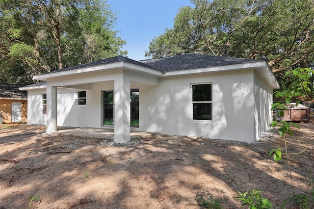 view of front facade with stucco siding, a patio, and a shingled roof