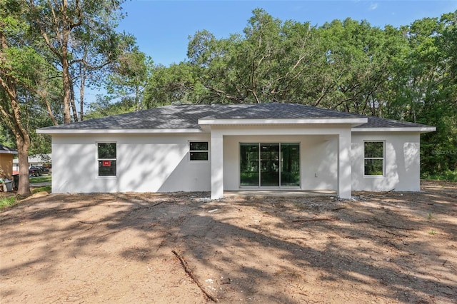 rear view of house with stucco siding and a shingled roof