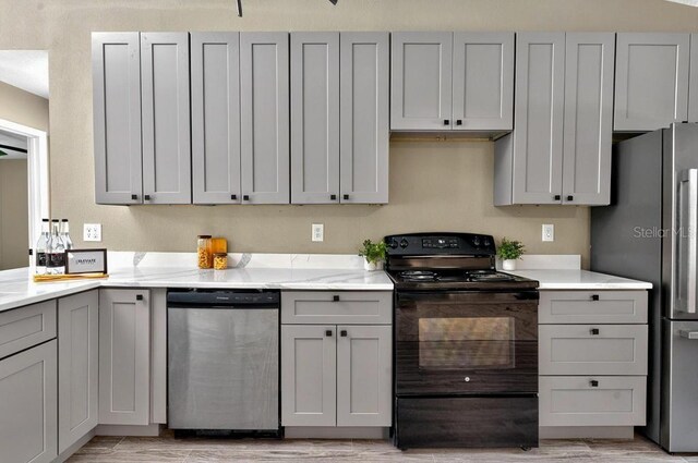 10545 Parkway Dr, Clermont, FL 34711 - kitchen featuring appliances with stainless steel finishes, gray cabinetry, light wood-type flooring, and light stone countertops