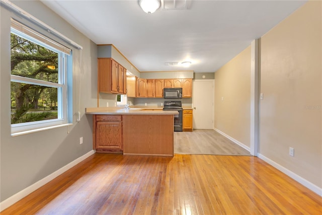 12046 SE 135th Ave, Ocklawaha, FL 32179 - kitchen with stove, black microwave, light wood-type flooring, light countertops, and a peninsula
