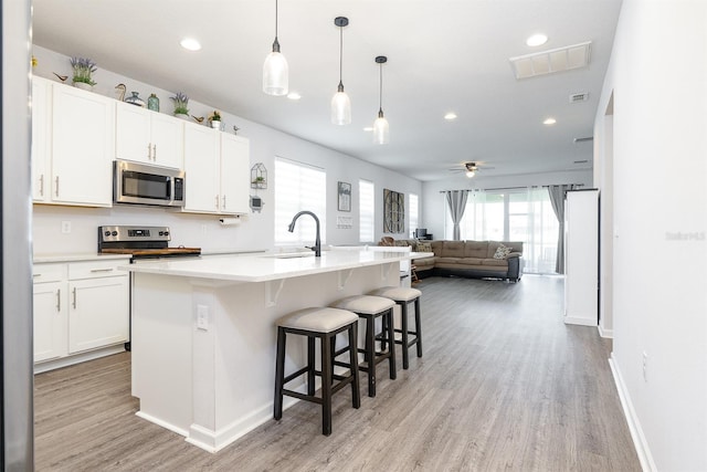 200 Summershore Dr, Auburndale, FL 33823 - kitchen with appliances with stainless steel finishes, a sink, light wood-style flooring, open floor plan, and white cabinetry