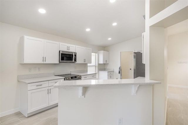 kitchen with appliances with stainless steel finishes, a peninsula, white cabinetry, a breakfast bar area, and recessed lighting