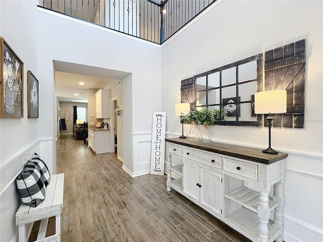 corridor with a wainscoted wall, wood finished floors, a decorative wall, and a high ceiling