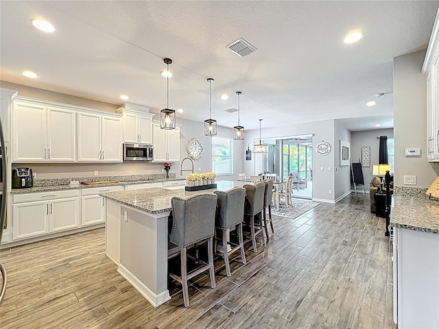 kitchen featuring stainless steel microwave, light wood-style floors, white cabinets, and recessed lighting