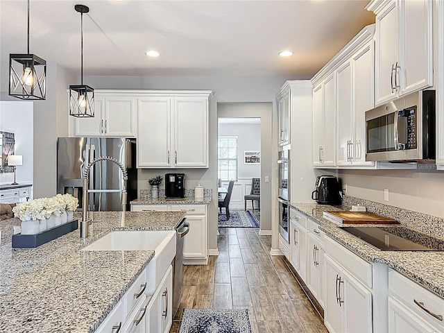 kitchen featuring stainless steel appliances, white cabinets, light wood-style floors, pendant lighting, and light stone countertops