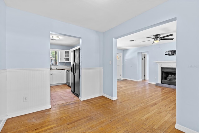 360 W University Ave, Orange City, FL 32763 - unfurnished living room featuring a wainscoted wall, light wood finished floors, a ceiling fan, a sink, and a brick fireplace