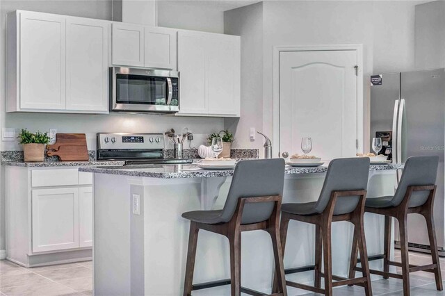 kitchen featuring appliances with stainless steel finishes, white cabinetry, stone countertops, a breakfast bar area, and light tile patterned flooring