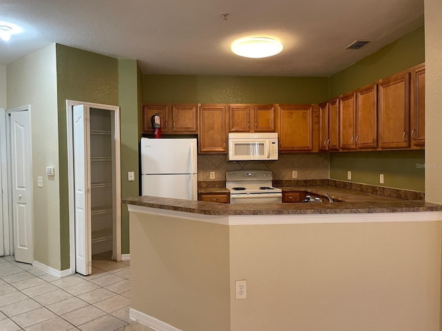 kitchen with white appliances, dark countertops, brown cabinets, and a peninsula