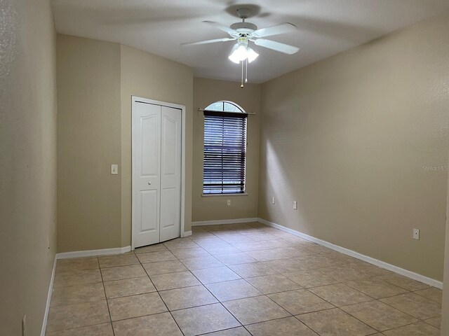 spare room with a ceiling fan, light tile patterned flooring, and baseboards