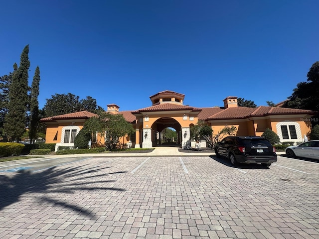 view of front facade with stucco siding, uncovered parking, a tile roof, and a chimney