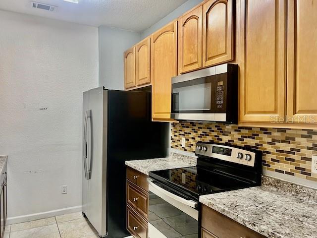 kitchen with appliances with stainless steel finishes, tasteful backsplash, light stone countertops, light tile patterned floors, and baseboards